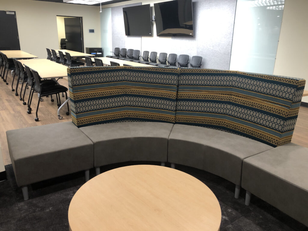 A meeting room with long individual tables for group activities in the background and lounge seating with a coffee table in the foreground